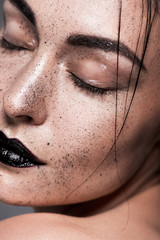 close up portrait of young woman with black lips and freckles on face, isolated on grey