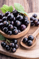 Fresh ripe black currant in wooden bowl with original leaves and spoon on rustic old background close-up