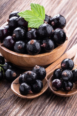 Fresh ripe black currant in wooden bowl with original leaves and two spoons on rustic old background