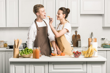 girlfriend feeding boyfriend with piece of bell pepper in kitchen