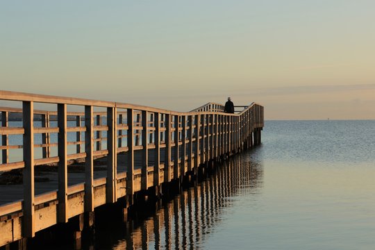 einsamer Mann steht alleine auf einer Seebrücke und blickt auf das Meer