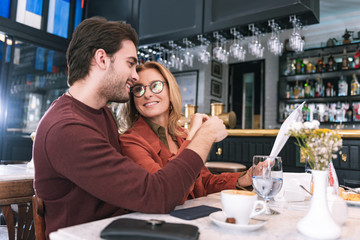Perfect date. Low angle of merry enthusiastic couple deciding on meal and sitting at table