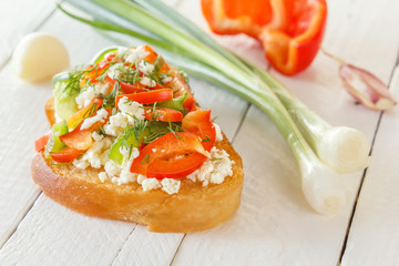 Bruschetta with red sweet pepper and goat cheese on a background of fresh vegetables on white boards. Close-up
