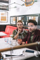 Age gap. Focused earnest woman touching face and man holding glass of wine