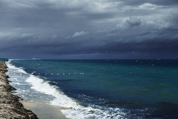 Fototapeta na wymiar Small waves with foam at the time of storm beginning in the evening on the shore of the dark sea on the beach of the sea resort