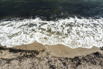 Small waves with foam at the time of storm beginning in the evening on the shore of the dark sea on the beach of the sea resort