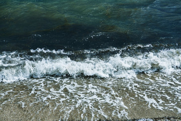 Fototapeta premium Small waves with foam at the time of storm beginning in the evening on the shore of the dark sea on the beach of the sea resort