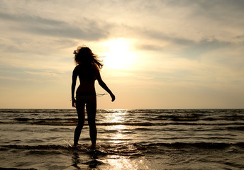 Fototapeta premium Silhouette of a young woman in sea at sunset.