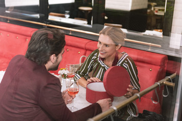 On our anniversary. Top view of amazed happy woman opening present and man drinking wine