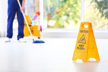 Safety sign with phrase Caution wet floor and blurred cleaner on background