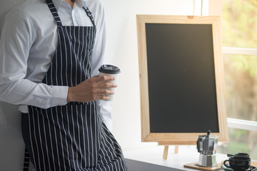 barista man holding cup of hot coffee to drink in cafeteria with copy space for text on advertisement board