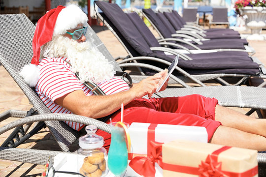 Authentic Santa Claus using tablet on lounge chair at resort