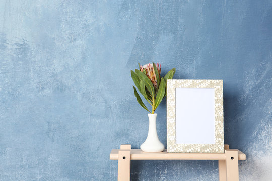 Blank frame and vase with flower on table near color wall. Mock up for design