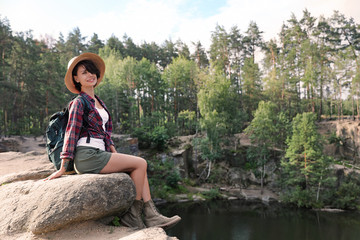 Fototapeta na wymiar Young woman on rock near lake and forest. Camping season
