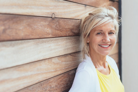 Smiling blond woman leaning on a wooden wall