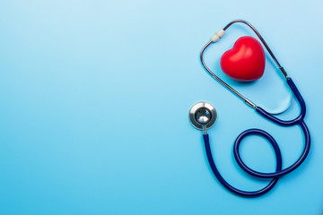 Stethoscope and red heart shape on blue background, top view design