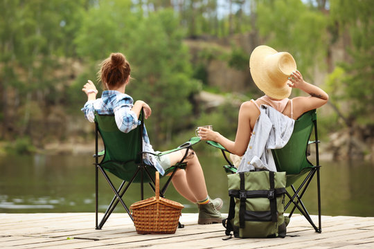 Young Friends Resting On Pier Near Lake. Camping Season