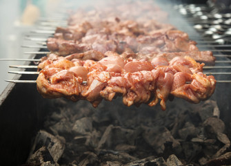 Grilled barbecue meat on skewers over fire with smoke cooking on a coal.