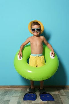 Cute little boy with inflatable ring wearing flippers near color wall