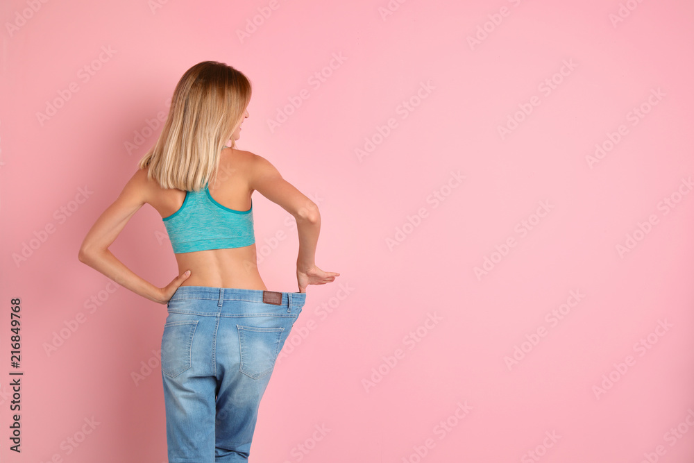 Canvas Prints Young slim woman in old big jeans showing her diet results on color background