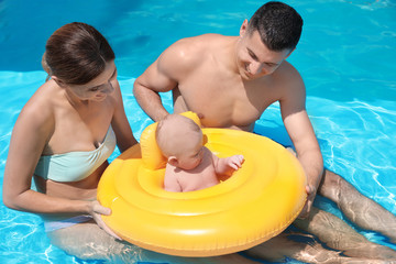 Happy parents with little baby in swimming pool on sunny day, outdoors