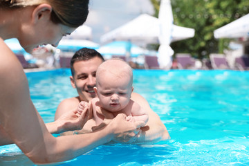 Fototapeta na wymiar Happy parents with little baby in swimming pool on sunny day, outdoors