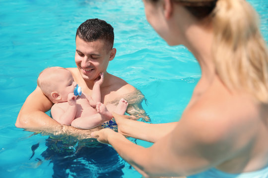 Happy parents with little baby in swimming pool on sunny day, outdoors