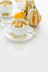 Two cups with fresh pumpkin cream soup decorated cream, seeds and crackers on white table cloth