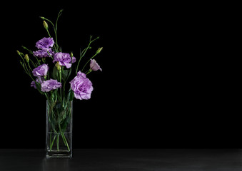 Vase with beautiful Eustoma flowers on table against dark background