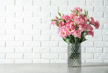 Vase with beautiful Eustoma flowers on table against brick wall
