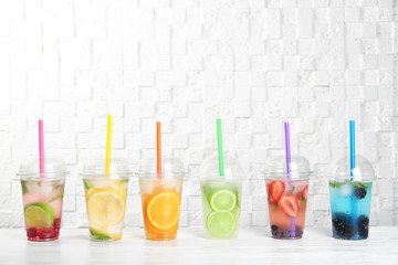 Plastic cups with lemonades on table near white wall