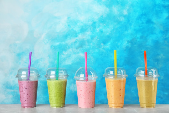 Plastic cups with smoothies on table against color background