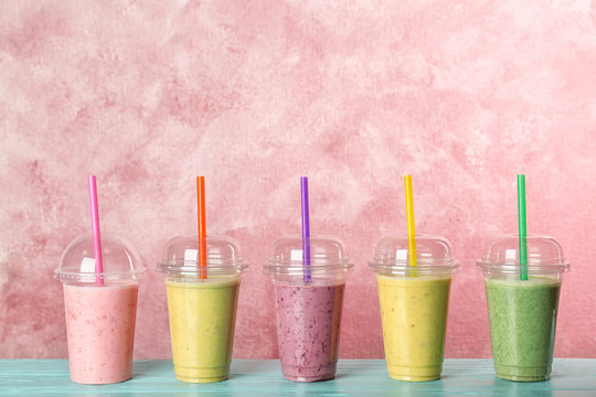 Plastic cups with smoothies on table against color background