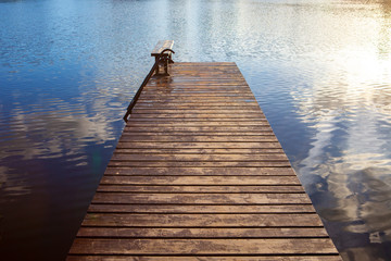 Beautiful wooden pier with clouds and sun reflected on calm and blue water