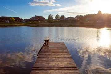 Beautiful wooden pier with clouds and sun reflected on calm and blue water