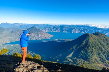 Rolgordijnen Hiker with panorama view of Lake Atitlan and volcano San Pedro and Toliman early in the morning from peak of volcano Atitlan, Guatemala. Hiking and climbing on Vulcano Atitlan. © Simon Dannhauer
