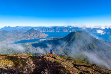 Hiker with panorama view of Lake Atitlan and volcano San Pedro and Toliman early in the morning from peak of volcano Atitlan, Guatemala. Hiking and climbing on Vulcano Atitlan.
