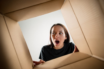 The surprised woman unpacking, opening carton box and looking inside. The package, delivery,...