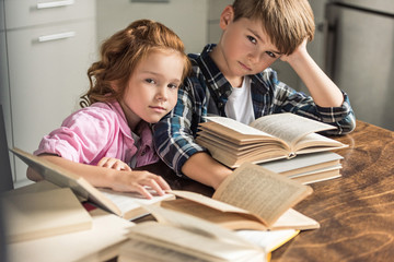little brother and sister sitting at table with pile of books and looking at camera
