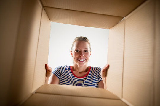 The surprised woman unpacking, opening carton box and looking inside. The package, delivery, surprise, gift, lifestyle concept. Human emotions and facial expressions concepts