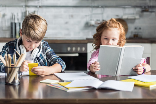 focused little siblings doing homework together at kitchen