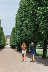 Obraz premium Young women relaxing during a summer day in a Danish park, perfectly manicured linden trees line an elegant garden alley. Concept of hygge.