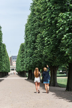 Young women relaxing during a summer day in a Danish park, perfectly manicured linden trees line an elegant garden alley. Concept of hygge.