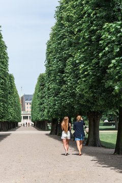 Young women relaxing during a summer day in a Danish park, perfectly manicured linden trees line an elegant garden alley. Concept of hygge.
