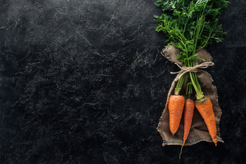 top view of fresh ripe carrots tied with rope on sackcloth on black marble surface