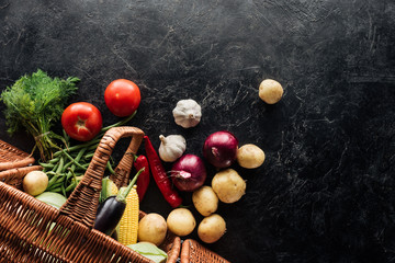 flat lay with various fresh vegetables in basket on black marble tabletop
