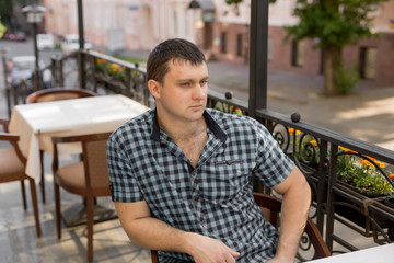 Fototapeta premium young man. the man in the shirt in the cage. portrait of a man. a man at a table in a cafe in the open area. 