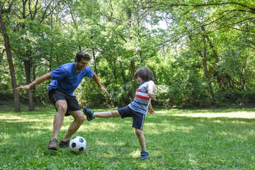 Father and son play with ball in autumn park. Happy family play soccer in public park