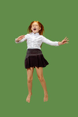 Young happy caucasian teen girl jumping in the air, isolated on green studio background. Beautiful female half-length portrait. Human emotions, facial expression concept.