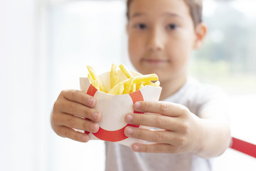 The boy 8 years old holds out the fries in paper box, fast food concept